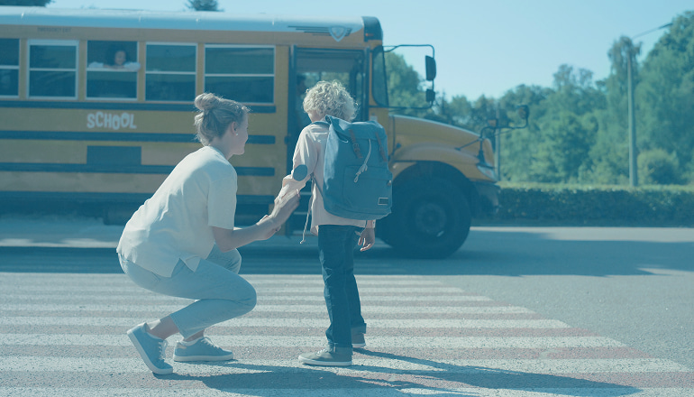 madre despidiendose de su hijo antes de subir al autobús escolar. Es importante saber los protocolos de actuación ante accidentes escolares en trayectos escolares